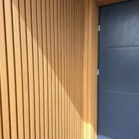 Lamel elewacyjny WPC w kolorze teak zamontowany na ścianie przy drzwiach wejściowych